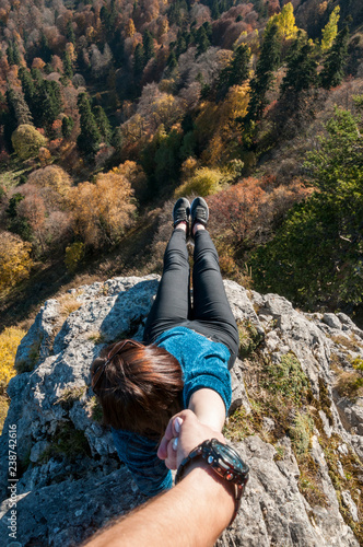 a young active girl sits on the edge of a rock, look at the Caucasus mountains.