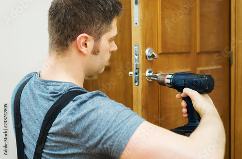 Young handyman in uniform changing door lock.