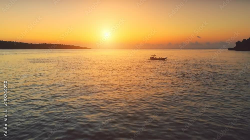 Drone Flight over Sunset Ocean. Boats sailing in soft orange light. Travel Vacation Recreation Paradise Tourism. Beautiful nature landscape in Tropical Nusa Penida Bali Island, Indonesia. 4K Zoom out