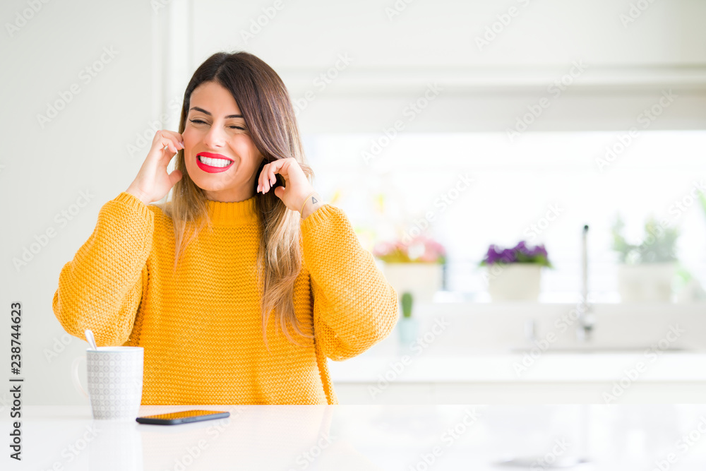 Young beautiful woman drinking a cup of coffee at home covering ears with fingers with annoyed expression for the noise of loud music. Deaf concept. Young beautiful woman drinking a cup of coffee at home covering ears with fingers with annoyed expression for the noise of loud music. Deaf concept.