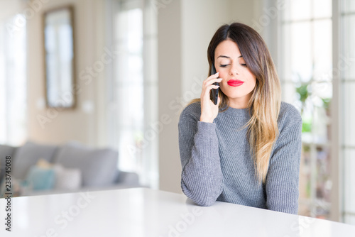 Young beautiful woman talking on the phone at home with a confident expression on smart face thinking serious
