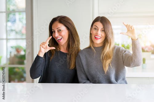 Beautiful family of mother and daughter together at home smiling and confident gesturing with hand doing size sign with fingers while looking and the camera. Measure concept. photo