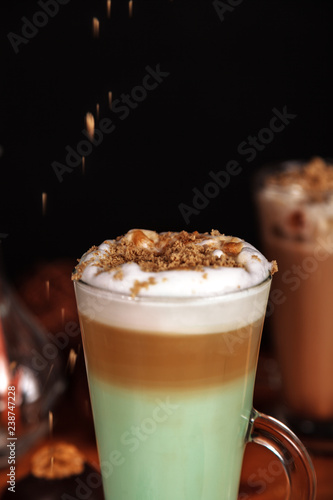 Coffee latte macchiato with mint syrup and whipped cream, sprinkled with chopped halva, in high transparent glasses, on a wooden table close-up, selective focus