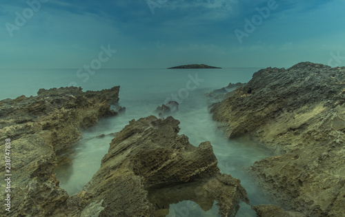Fototapeta Naklejka Na Ścianę i Meble -  Mallorca, Balearic Islands, Spain - October 27, 2018: Long exposure on a rocky beach at low tide, with a small island in the background