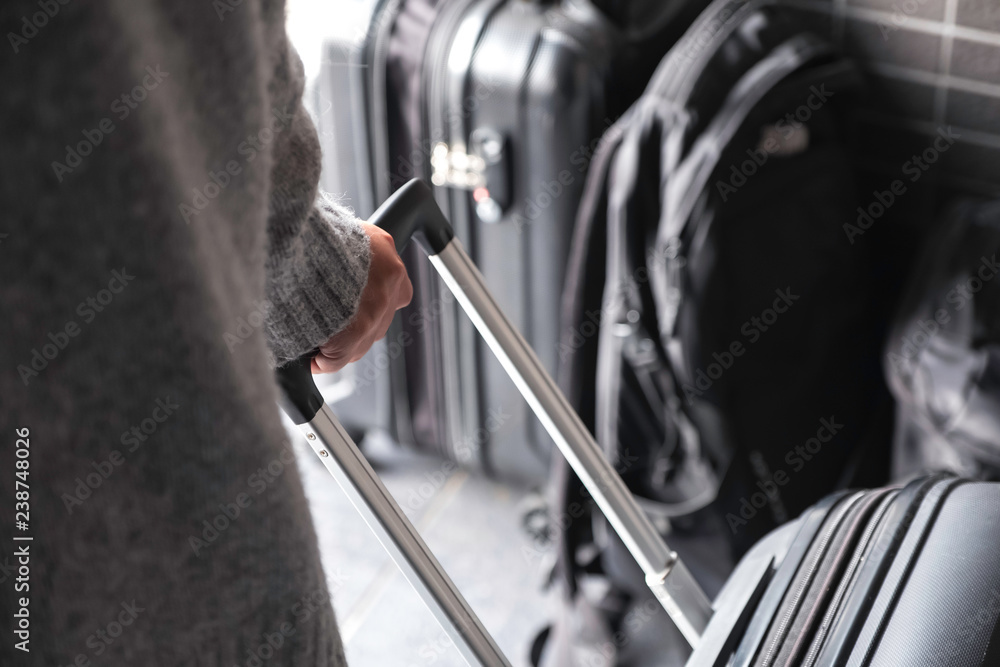 Closeup image of a woman holding and dragging a black baggage for traveling in the outdoors Closeup image of a woman holding and dragging a black baggage for traveling in the outdoors