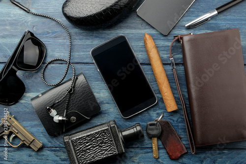 Men's Accessories.men's style. Glasses, business card holder, cigar, smartphone, notebook, headphones, and a pistol-lighter on a blue wooden background. Lay lay.