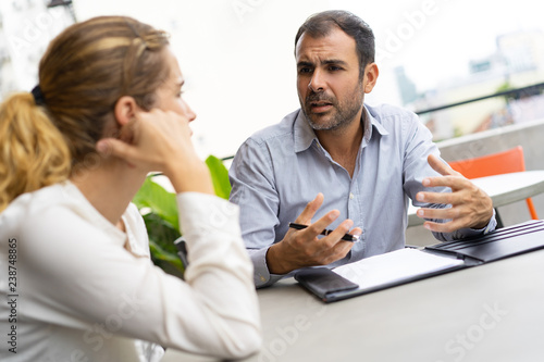 Business team reviewing documents and discussing project. Business colleagues arguing at outdoor cafe table. Arguing concept