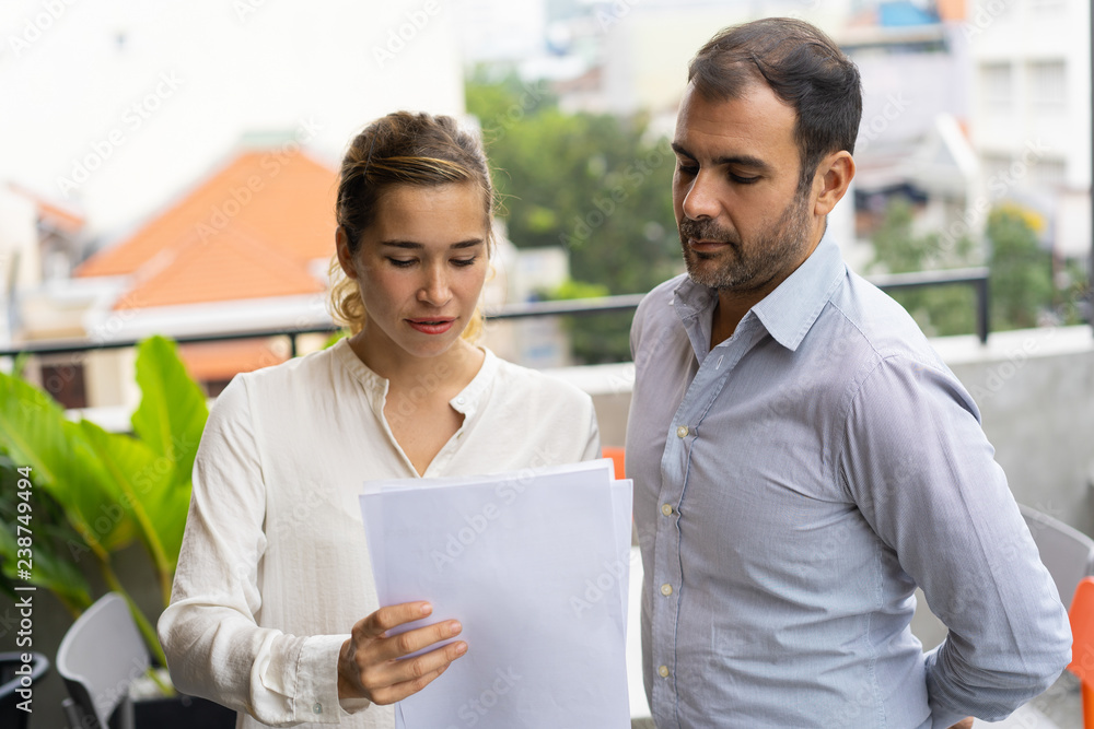 Pensive young employee consulting mentor during break. Business man and woman discussing documents outside. Consulting concept Pensive young employee consulting mentor during break. Business man and woman discussing documents outside. Consulting concept