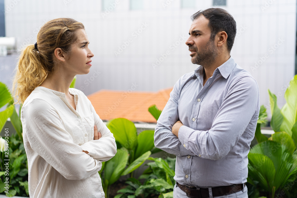 Serious business colleagues arguing about project during break. Frowning male and female employees keeping arms crossed and talking to each other. Arguing concept Serious business colleagues arguing about project during break. Frowning male and female employees keeping arms crossed and talking to each other. Arguing concept