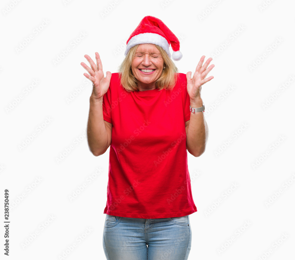 Middle age blonde woman wearing christmas hat over isolated background celebrating mad and crazy for success with arms raised and closed eyes screaming excited. Winner concept Middle age blonde woman wearing christmas hat over isolated background celebrating mad and crazy for success with arms raised and closed eyes screaming excited. Winner concept