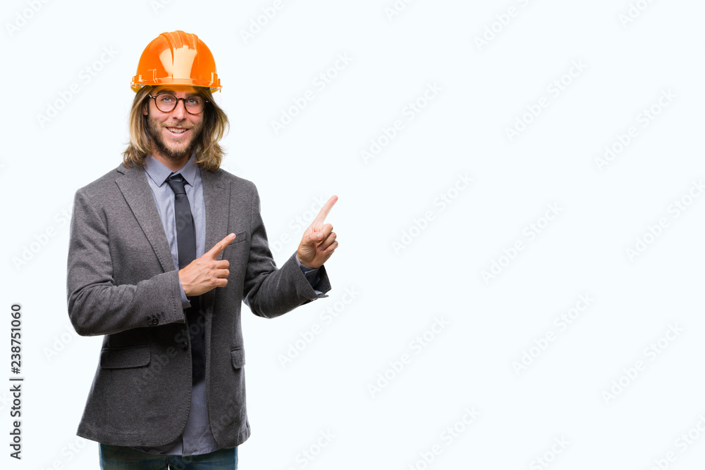 Young handsome architec man with long hair wearing safety helmet over isolated background smiling and looking at the camera pointing with two hands and fingers to the side. Young handsome architec man with long hair wearing safety helmet over isolated background smiling and looking at the camera pointing with two hands and fingers to the side.