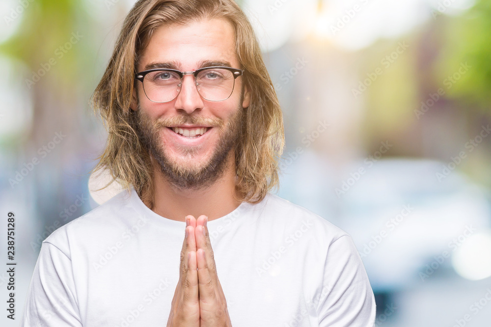 Young handsome man with long hair wearing glasses over isolated background praying with hands together asking for forgiveness smiling confident. Young handsome man with long hair wearing glasses over isolated background praying with hands together asking for forgiveness smiling confident.
