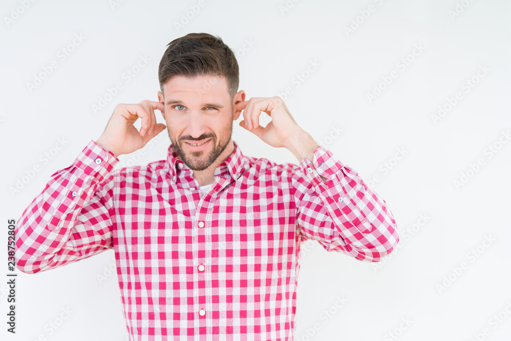 Young handsome man wearing shirt over isolated background covering ears with fingers with annoyed expression for the noise of loud music. Deaf concept. Young handsome man wearing shirt over isolated background covering ears with fingers with annoyed expression for the noise of loud music. Deaf concept.