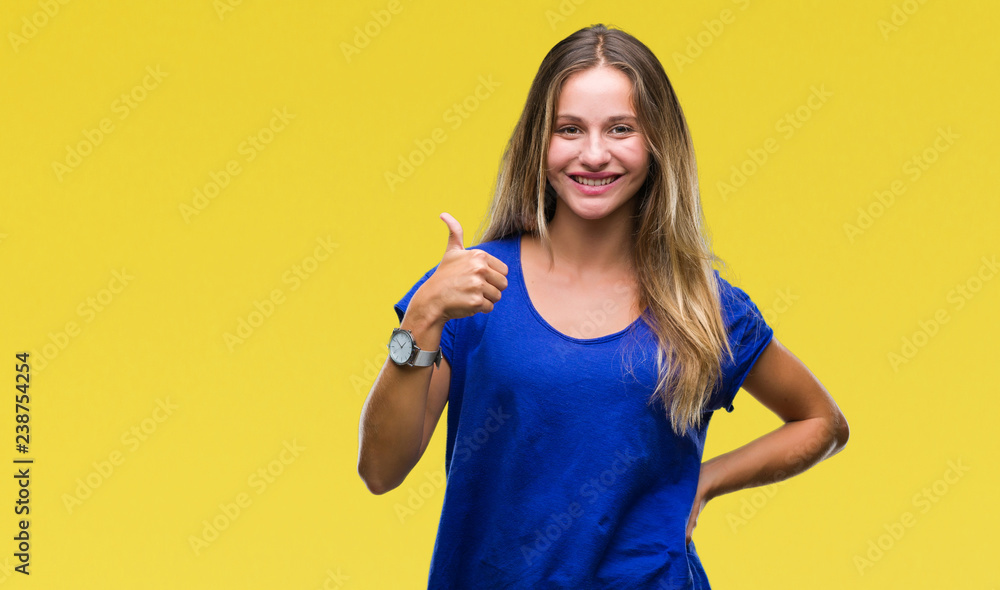 Young beautiful blonde woman over isolated background doing happy thumbs up gesture with hand. Approving expression looking at the camera with showing success. Young beautiful blonde woman over isolated background doing happy thumbs up gesture with hand. Approving expression looking at the camera with showing success.