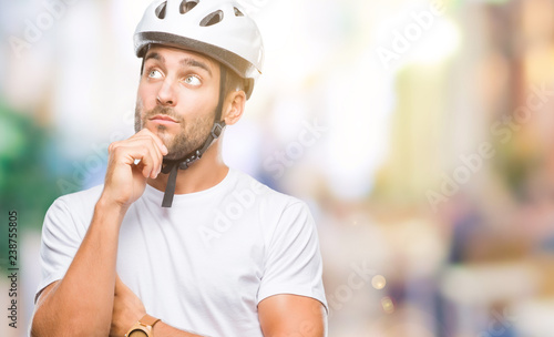 Young handsome man wearing cyclist safety helmet over isolated background with hand on chin thinking about question, pensive expression. Smiling with thoughtful face. Doubt concept.