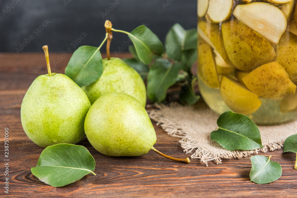 Homemade pear compote and fresh pears with leaves on dark wooden background.