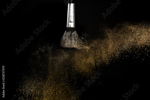 gold powder splash and brush for makeup artist or graphic design in black background, look like a luxury mood