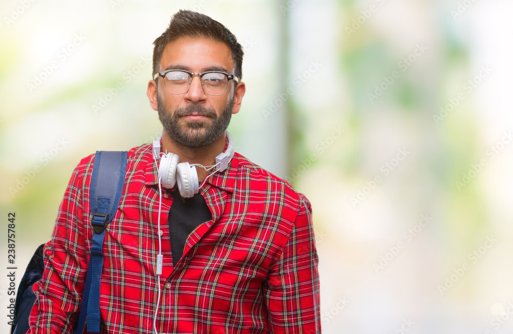 Adult hispanic student man wearing headphones and backpack over isolated background with serious expression on face. Simple and natural looking at the camera. Adult hispanic student man wearing headphones and backpack over isolated background with serious expression on face. Simple and natural looking at the camera.