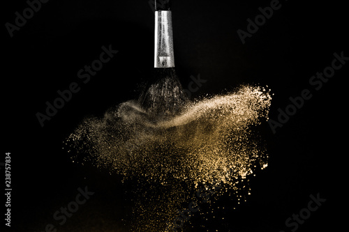 gold powder splash and brush for makeup artist or graphic design in black background, look like a luxury mood