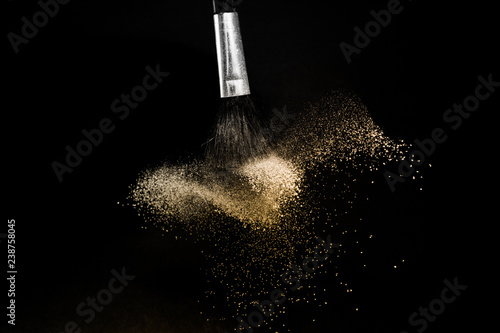 gold powder splash and brush for makeup artist or graphic design in black background, look like a luxury mood