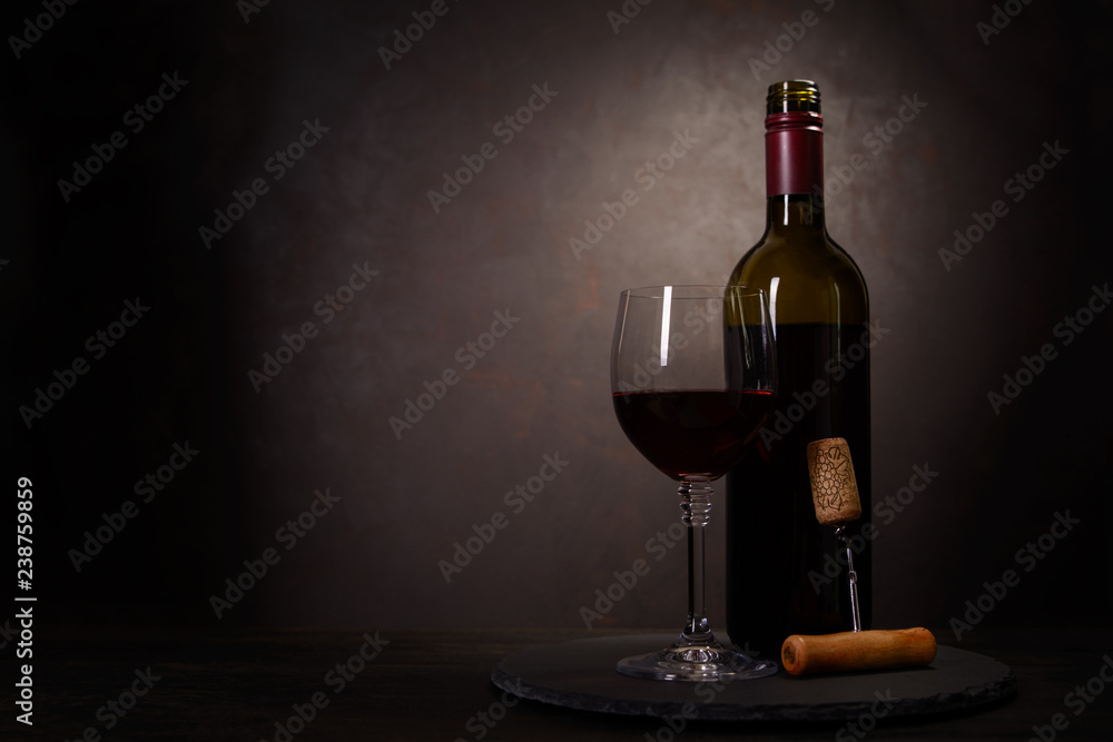 Fototapeta premium Wine bottle, glass with red wine and cork with corkscrew on dark wooden background. Celebration concept. Copy space