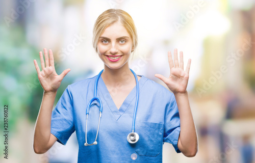 Young beautiful blonde doctor surgeon nurse woman over isolated background showing and pointing up with fingers number ten while smiling confident and happy.