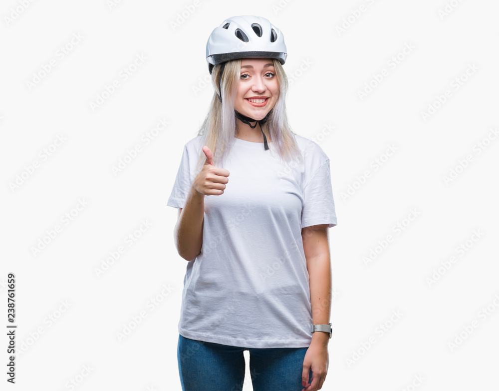 Young blonde woman wearing cyclist security helmet over isolated background doing happy thumbs up gesture with hand. Approving expression looking at the camera with showing success. Young blonde woman wearing cyclist security helmet over isolated background doing happy thumbs up gesture with hand. Approving expression looking at the camera with showing success.