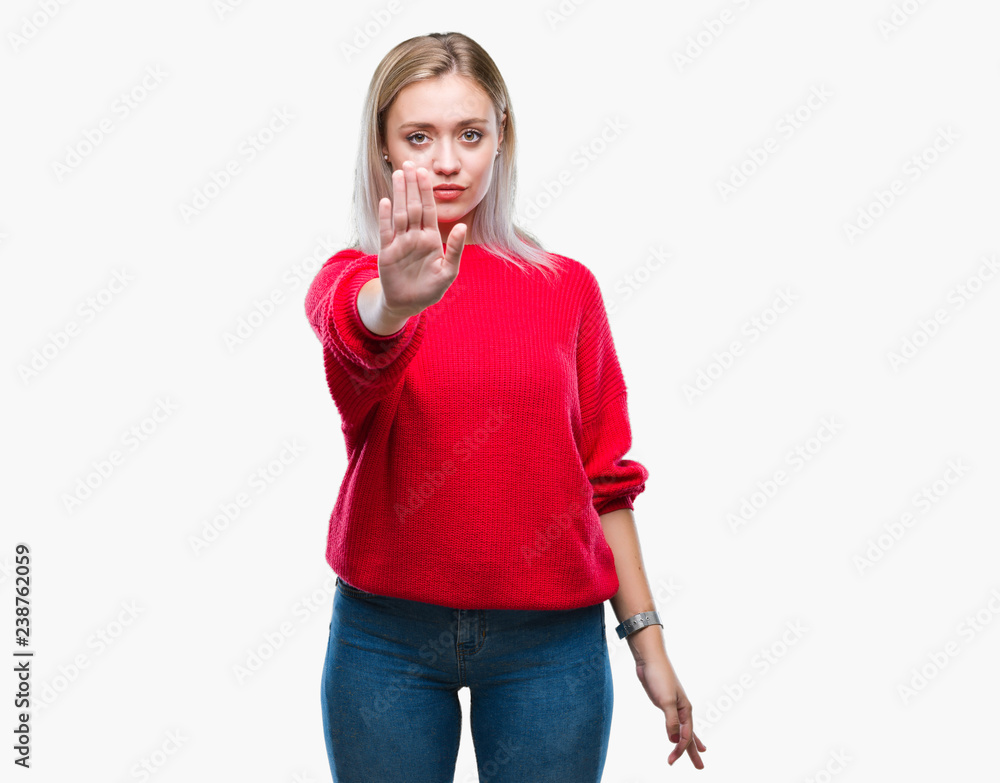 Young blonde woman wearing winter sweater over isolated background doing stop sing with palm of the hand. Warning expression with negative and serious gesture on the face. Young blonde woman wearing winter sweater over isolated background doing stop sing with palm of the hand. Warning expression with negative and serious gesture on the face.