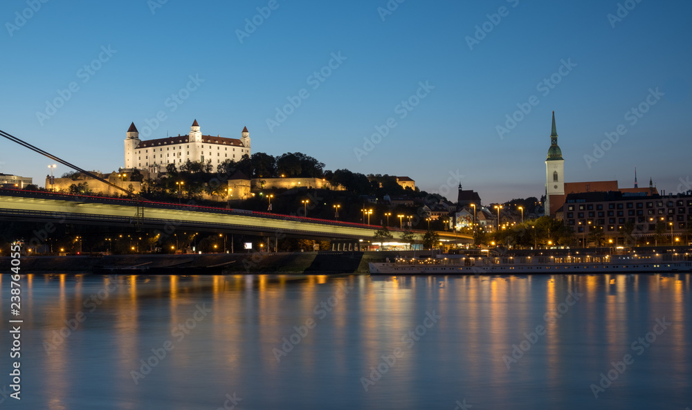 Night time view of the skyline of Bratislava from the shore of the Danube river.  View of the UFO bridge, the castle and the old town. 
