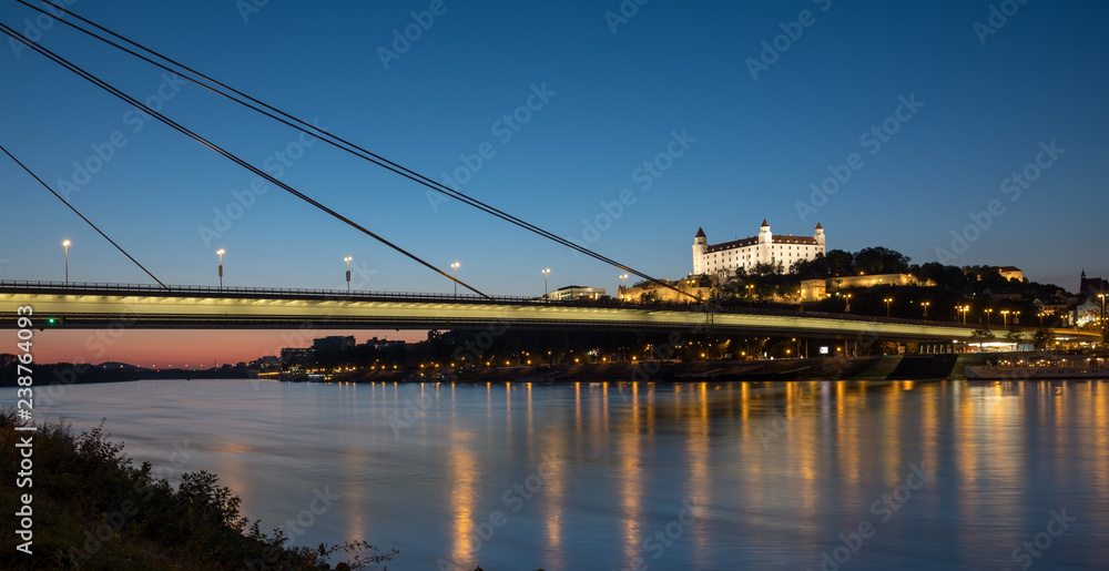 Night time view of the skyline of Bratislava from the shore of the Danube river.  View of the UFO bridge, the castle and the old town. 