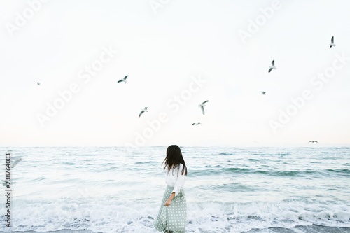 Marine female portrait. Attractive woman in green skirt walks along the shore before the sea while gulls fly over her