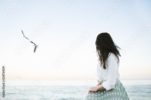 Marine female portrait. Attractive woman in green skirt walks along the shore before the sea while gulls fly over her