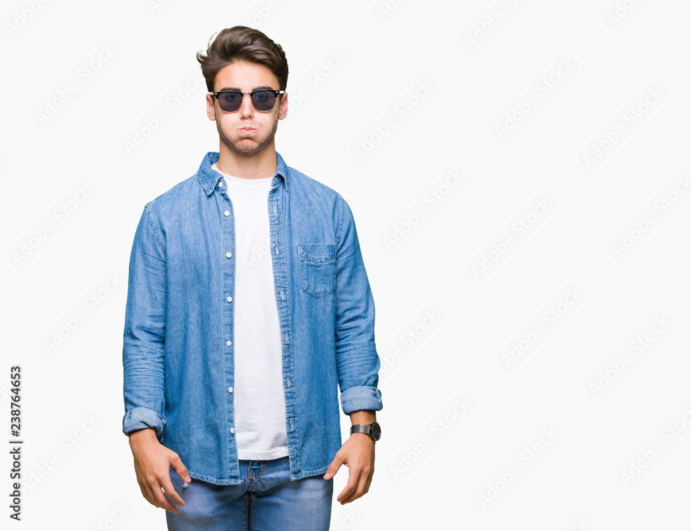 Fototapeta premium Young handsome man wearing sunglasses over isolated background puffing cheeks with funny face. Mouth inflated with air, crazy expression.