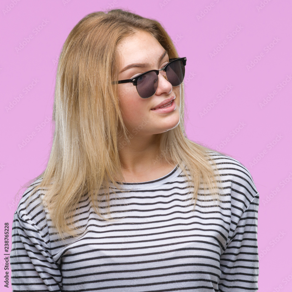 Young caucasian woman wearing sunglasses over isolated background looking away to side with smile on face, natural expression. Laughing confident. Young caucasian woman wearing sunglasses over isolated background looking away to side with smile on face, natural expression. Laughing confident.