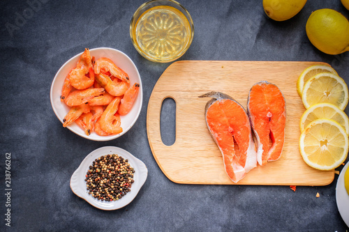 Wooden board in the middle of the frame with the salmon laid out in a plate raw shrimp pepper lemon slices with seasoning oil.
