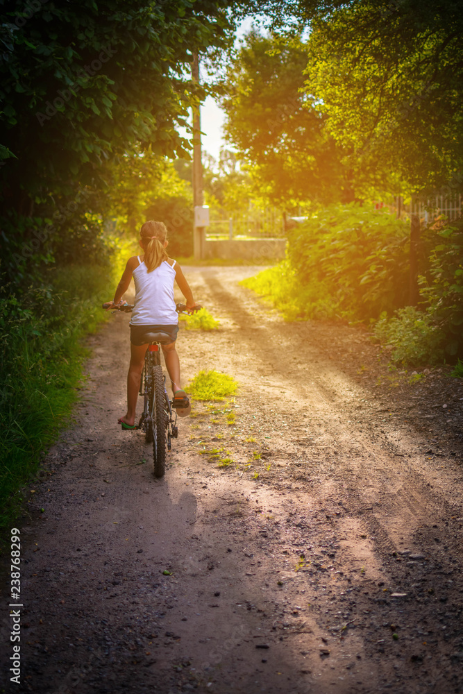 Fototapeta premium Childhood bliss: girl happily riding a bicycle on a rural dirt road