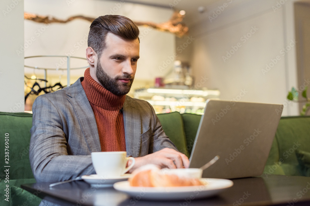 focused handsome businessman in formal wear sitting at table and typing on laptop in restaurant focused handsome businessman in formal wear sitting at table and typing on laptop in restaurant
