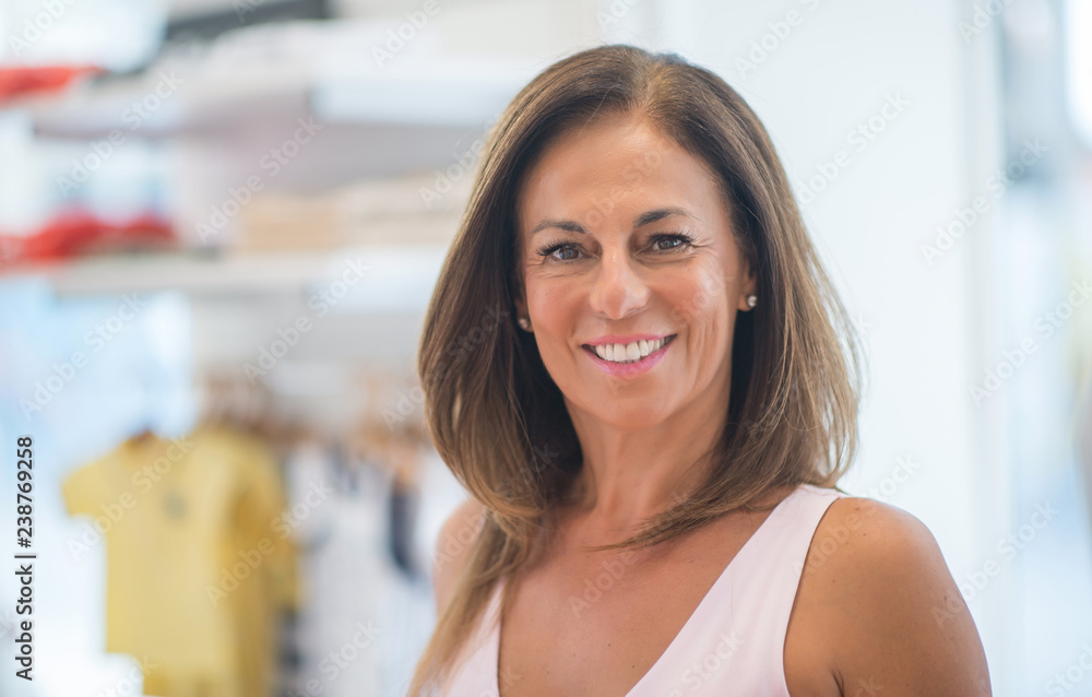 Beautiful middle age hispanic woman standing with smile on face at clothes store. Shop owner and shop assistant smiling confident and cheerful