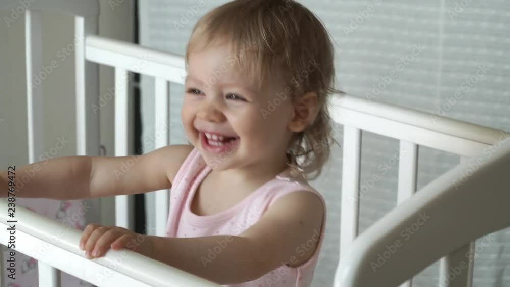 Little pretty girl with blond curly hair in a white crib laughing and smiling Little pretty girl with blond curly hair in a white crib laughing and smiling