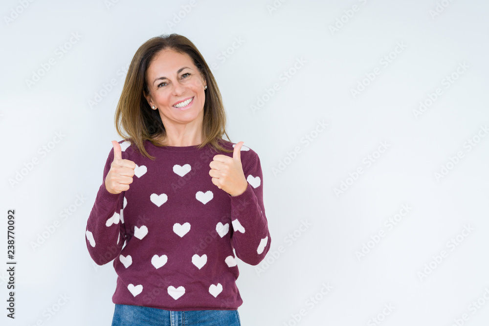 Beautiful middle age woman wearing heart sweater over isolated background success sign doing positive gesture with hand, thumbs up smiling and happy. Looking at the camera with cheerful expression Beautiful middle age woman wearing heart sweater over isolated background success sign doing positive gesture with hand, thumbs up smiling and happy. Looking at the camera with cheerful expression