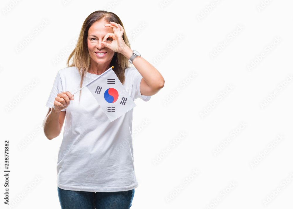Middle age hispanic woman holding flag of South Korea over isolated background with happy face smiling doing ok sign with hand on eye looking through fingers Middle age hispanic woman holding flag of South Korea over isolated background with happy face smiling doing ok sign with hand on eye looking through fingers