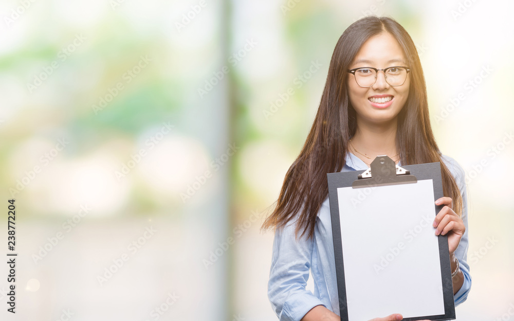 Young asian business woman holding clipboard over isolated background with a happy face standing and smiling with a confident smile showing teeth Young asian business woman holding clipboard over isolated background with a happy face standing and smiling with a confident smile showing teeth