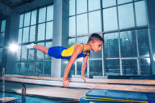 The little boy is engaged in sports gymnastics on a parallel bars at gym. The performance, sport, acrobat, acrobatic, exercise, training concept