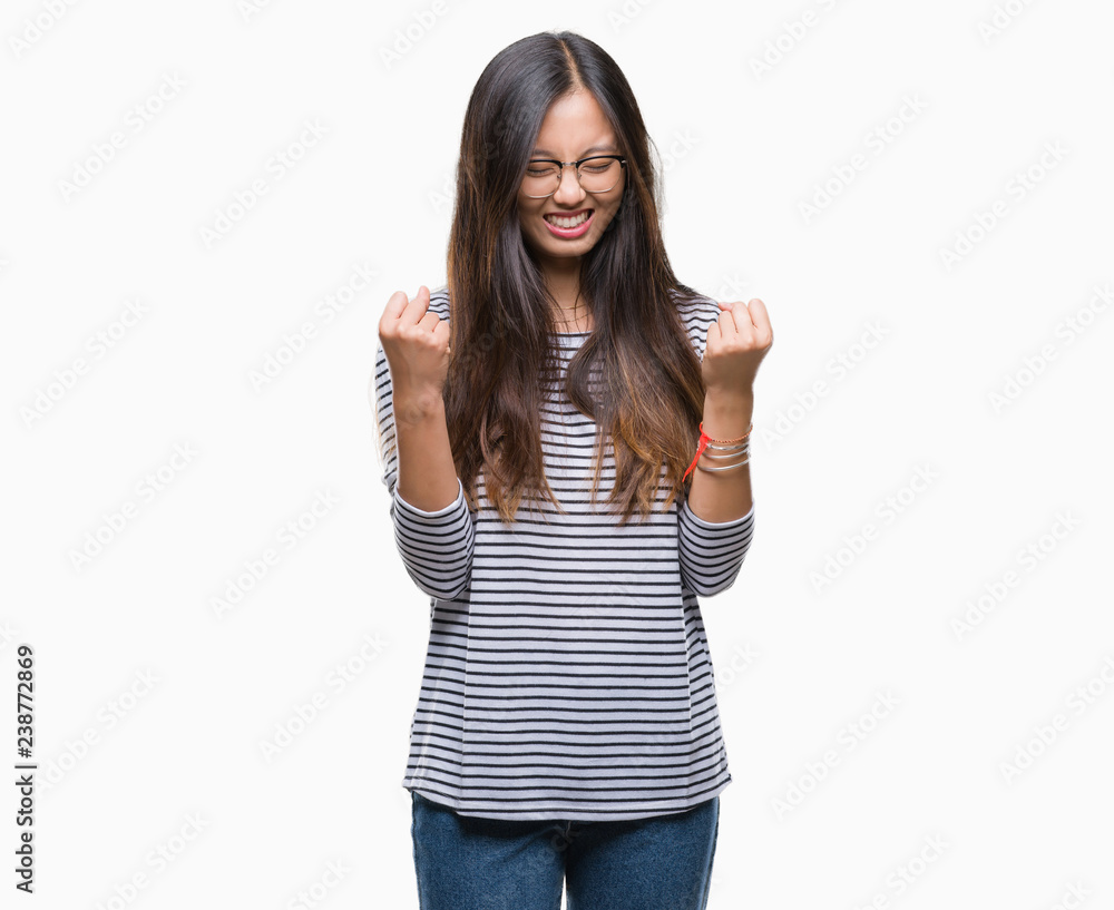 Young asian woman wearing glasses over isolated background very happy and excited doing winner gesture with arms raised, smiling and screaming for success. Celebration concept. Young asian woman wearing glasses over isolated background very happy and excited doing winner gesture with arms raised, smiling and screaming for success. Celebration concept.
