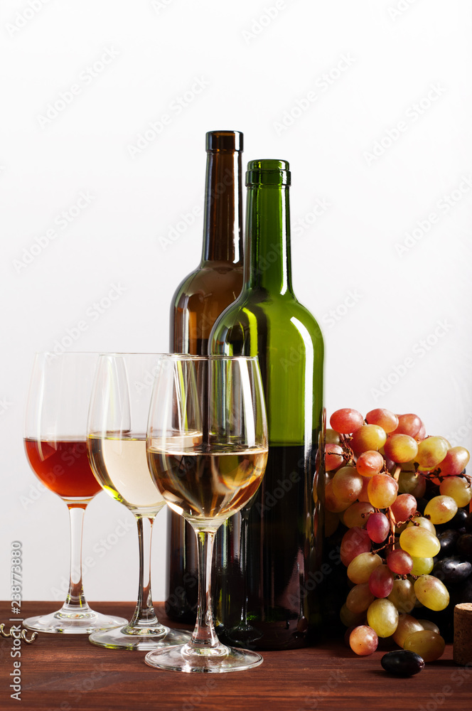 Wine in bottles and glasses on a brown wooden board. White  background. Next to the grapes. Author's retouching, selective sharpness