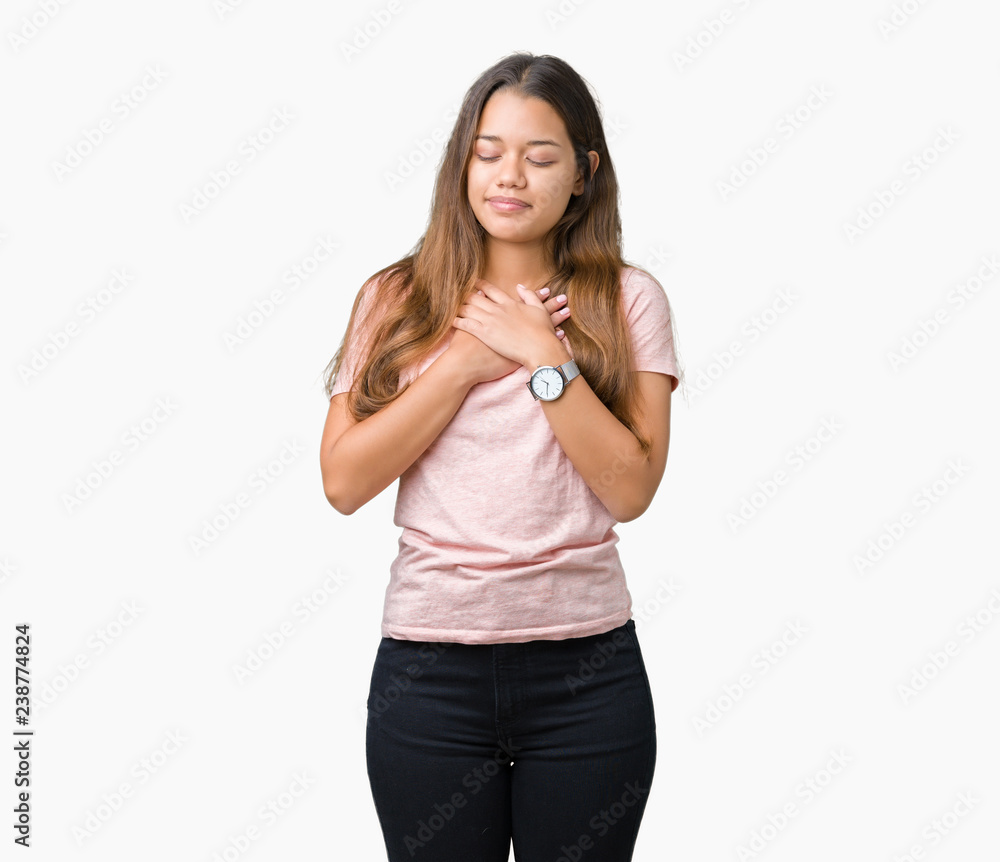 Young beautiful brunette woman wearing pink t-shirt over isolated background smiling with hands on chest with closed eyes and grateful gesture on face. Health concept. Young beautiful brunette woman wearing pink t-shirt over isolated background smiling with hands on chest with closed eyes and grateful gesture on face. Health concept.