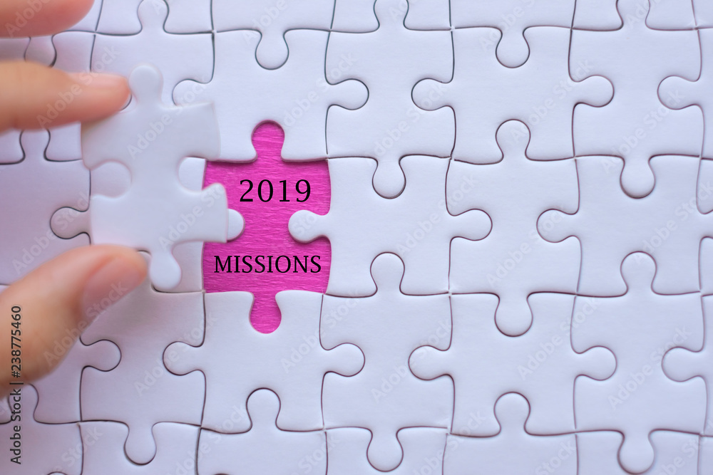 Woman Hand holding white jigsaw puzzle piece with words 2019 MISSION. Business resolutions, success, goals, New Year New Start and strategy concept Woman Hand holding white jigsaw puzzle piece with words 2019 MISSION. Business resolutions, success, goals, New Year New Start and strategy concept