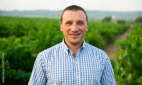 Male farmer standing near grapes in vineyard at summertime