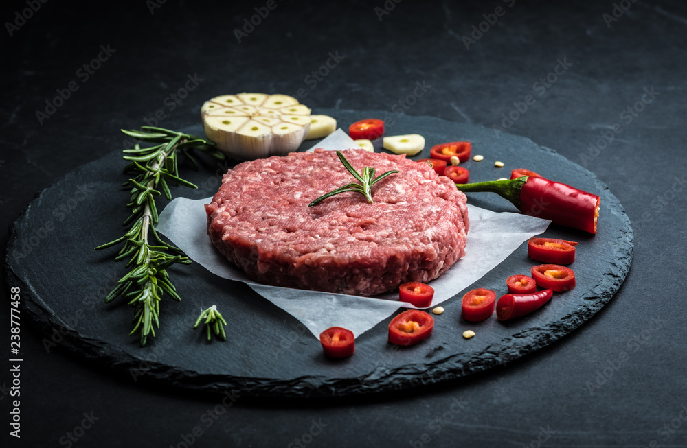 Raw ground beef meat burger steak cutlet with chili, rosemary and garlic on black slate plate for cooking Raw ground beef meat burger steak cutlet with chili, rosemary and garlic on black slate plate for cooking