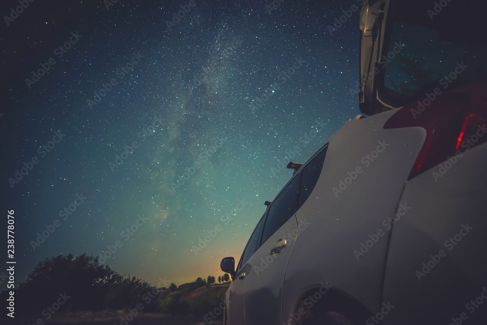 Car under the stars of the milky way in the night sky. White car
